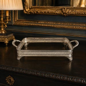 May include: A rectangular silver-toned serving tray featuring an intricate openwork lattice pattern along the sides. The tray is supported by four ornate feet and includes two curved handles on opposite ends, showcasing a polished metallic finish.
