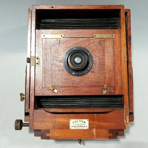 May include: A vintage wooden camera with a large lens and bellows. The camera has brass hardware and a small metal plate that reads "R.O.C. View, Eastman Kodak Co., Rochester Optical Co., Rochester, N.Y."