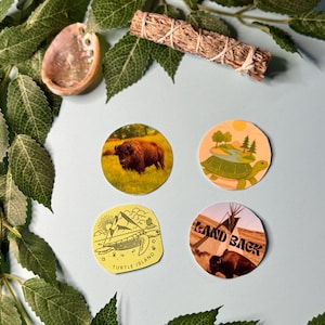 May include: A collection of round stickers featuring nature-themed designs. One sticker shows a bison in a field, another a turtle with a landscape, and a third with the text "Turtle Island". Also included are a sage bundle and an abalone shell.