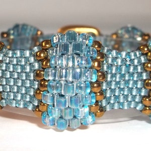 May include: A blue and gold beaded bracelet with a geometric design. The bracelet is made with small, square beads in a light blue color and round gold beads.