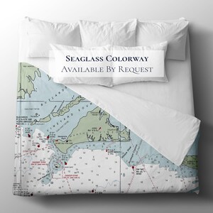 May include: A nautical-themed bedding set featuring a map design in shades of blue, green, and white. The text "SEAGLASS COLORWAY AVAILABLE BY REQUEST" is displayed on the pillowcases. The bedding is on a white bed.