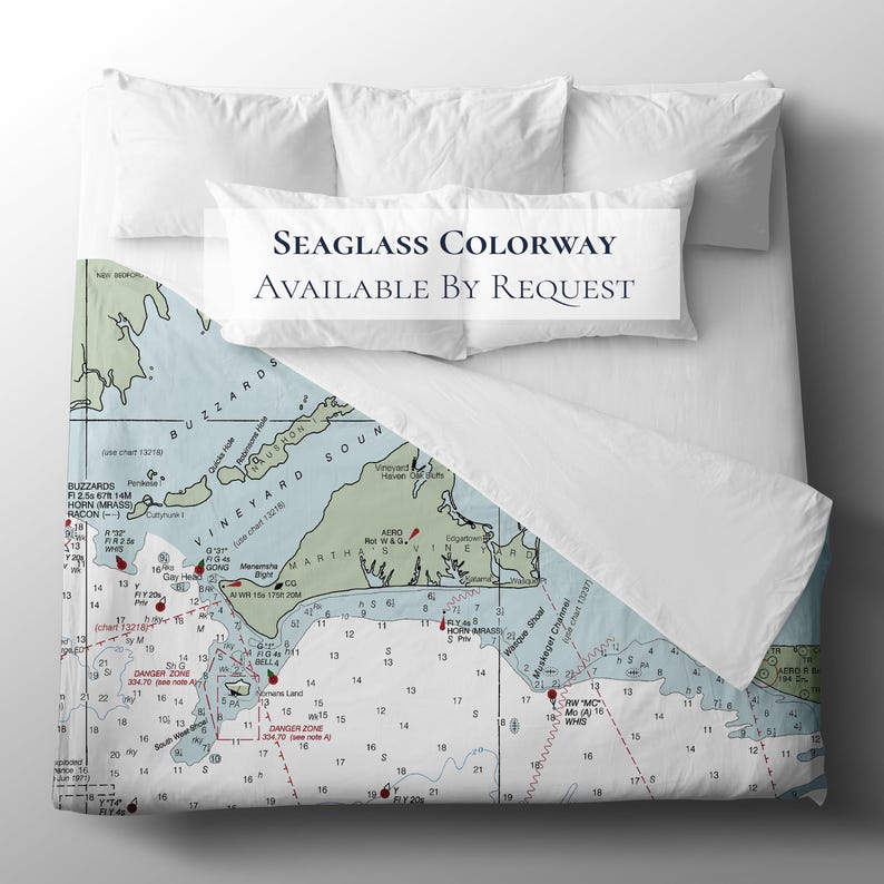 May include: A nautical-themed bedding set featuring a map design in shades of blue, green, and white. The text "SEAGLASS COLORWAY AVAILABLE BY REQUEST" is displayed on the pillowcases. The bedding is on a white bed.