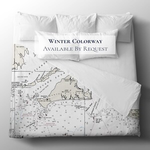 May include: White bedding set with a nautical chart design. The duvet cover features a detailed map of an island with text that reads "Winter Colorway Available By Request". Includes two standard pillows and a bolster pillow.