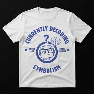 Puede incluir: Camiseta blanca con un diseño azul. El diseño presenta una cabeza de robot con gafas, un signo de interrogación y las palabras "Currently Decoding Symbolism". El texto adicional incluye "Error 404" y "Brain Loading".