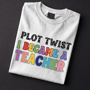 Puede incluir: Camiseta blanca de cuello redondo con el texto "PLOT TWIST I BECAME A TEACHER" en letras coloridas y en negrita. El texto está dispuesto en dos líneas, con las palabras "PLOT TWIST" en negro con estrellas blancas.