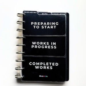 May include: A black disc-bound planner with three clear plastic dividers labeled PREPARING, WIPS, and COMPLETED. The pages feature white text reading PREPARING TO START, WORKS IN PROGRESS, and COMPLETED WORKS, with the brand name DRILL&REVEAL at the bottom.