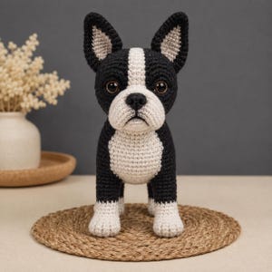 May include: A crochet Boston Terrier dog figurine featuring a black and white color scheme. The plush toy has large dark brown eyes, pointed ears with light beige inner details, and a white muzzle, chest, and paws against a black body.