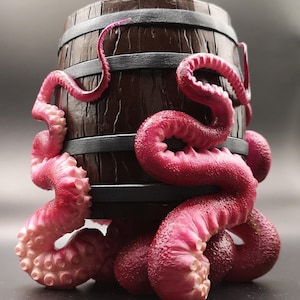 Puede incluir: Un barril de madera marrón oscuro con una banda de metal negro está envuelto en tentáculos de pulpo rosa. Los tentáculos están enroscados alrededor del barril y forman una base para que el barril se mantenga de pie.