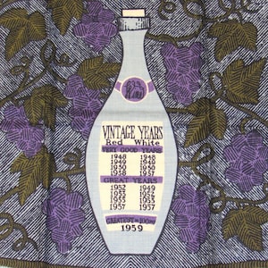 May include: A light blue kitchen towel with a wine bottle design and the text "VINTAGE YEARS". The towel features purple grapes and green leaves. The text lists vintage years for red and white wines.