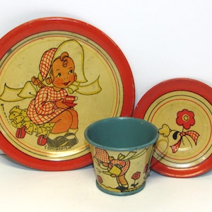May include: Vintage children's tin tea set with a red and yellow color scheme. The set includes a large plate, a small plate, and a cup. The plates feature illustrations of a girl and a dog. The cup is teal.