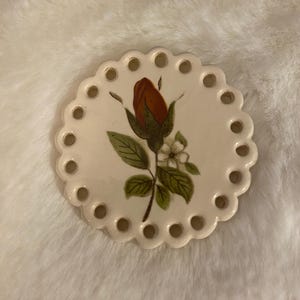 May include: A white ceramic mug with a black handle and the text "But First, Coffee" in a bold, black font. The mug is set against a blurred background, suggesting a cozy setting.