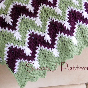 May include: A crocheted blanket with a scalloped edge in shades of green, purple, and white. The blanket is made with a repeating square pattern. The text "Susan J Patterns" is visible in the lower right corner of the image.