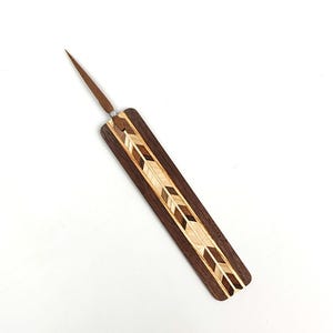 May include: A handcrafted wooden awl with a dark brown handle and a decorative inlaid design featuring light and dark wood chevron patterns. The awl has a pointed metal tip and a small silver accent near the handle.