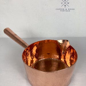 May include: A hammered copper saucepan with a long handle and a pouring spout. The interior and exterior feature a metallic copper finish. The logo for Copper & Wood Vintage is visible in the upper right corner, featuring the letters C and W.