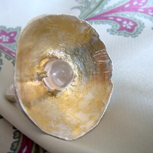 May include: A gold ring with a clear quartz stone set in the center. The ring is made of metal and has a textured surface.