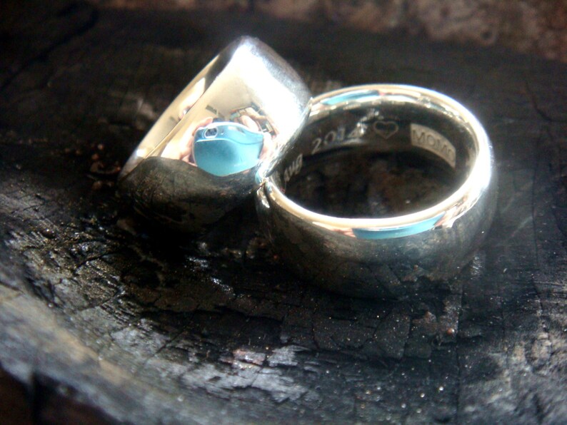 May include: Two silver wedding bands, one with a heart and the inscription "2014" and the other with a smooth surface.
