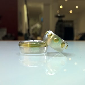 May include: Two silver rings with gold accents. One ring has a textured surface with gold dots, while the other has a thin gold band.
