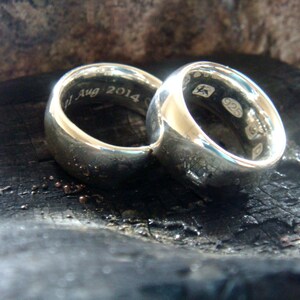 May include: Two silver wedding bands with a rounded profile. The band on the left has the inscription "1 Aug 2014". The band on the right has the inscription "925".