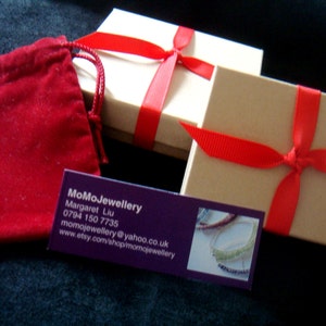 May include: Two brown gift boxes tied with red ribbon. The boxes are sitting on a dark blue surface. A red velvet bag and a business card are also visible. The business card reads "MoMoJewellery, Margaret Liu, 0794 150 7735, momojewellery@yahoo.co.uk, www.etsy.com/shop/momojewellery".