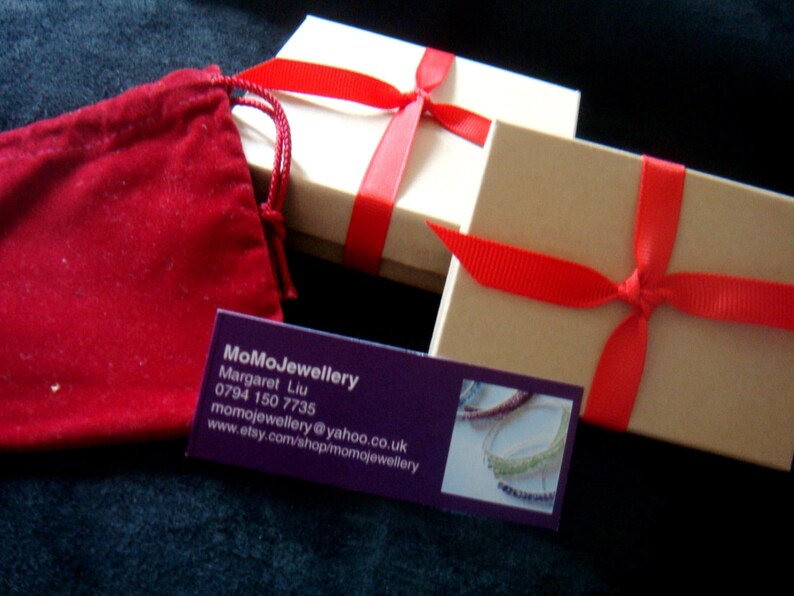 May include: Two brown gift boxes tied with red ribbon. The boxes are sitting on a dark blue surface. A red velvet bag and a business card are also visible. The business card reads "MoMoJewellery, Margaret Liu, 0794 150 7735, momojewellery@yahoo.co.uk, www.etsy.com/shop/momojewellery".