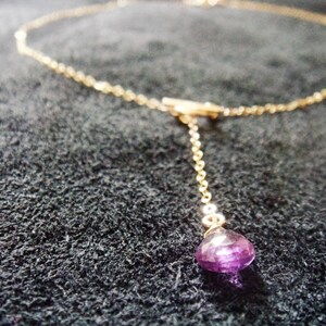 May include: A delicate gold chain necklace with a single purple gemstone pendant.