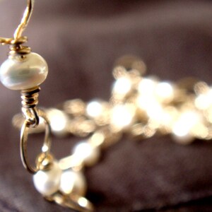 May include: A gold chain necklace with white pearl beads. The necklace is made of wire and has a simple design.