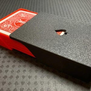 Peut inclure: Un jeu de cartes à jouer dans un étui en deux parties. Le plateau intérieur est rouge vif, tandis que le manchon extérieur est noir texturé avec une petite découpe en forme de pique sur le dessus révélant le dos rouge de la carte.