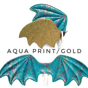 May include: A pair of dragon wings, one set is gold with a glitter finish, the other is a teal blue with a shimmery finish. The wings are labeled "Aqua Print/Gold".