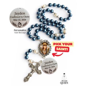 May include: A rosary with navy blue beads and white pearl accents. The rosary features a silver crucifix and a pendant with an image of a saint. Two silver pendants are engraved with the name "Jayden" and the date "May 22, 2026". The text "Pick Your Saint!" is also visible.