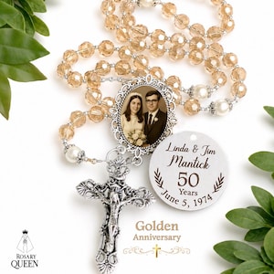 May include: A rosary featuring light amber faceted beads, white pearl accents, and a silver-toned crucifix. A central oval pendant displays a vintage black and white wedding photograph. A round silver charm is engraved with Linda & Jim Mantick 50 Years June 5, 1974.