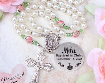 May include: A rosary featuring white pearl beads, small green crystal accents, and pink floral beads. It includes a silver-toned crucifix, a Miraculous Medal, and a round metal disc engraved with the text Mila, Baptized in Christ, September 15, 2024.