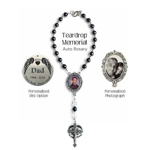 May include: A memorial auto rosary with black beads, a photo pendant, and a cross pendant. The rosary includes a personalized disc option with the text "Dad" and the years 1964-2018. The text "Teardrop Memorial Auto Rosary" is also visible.
