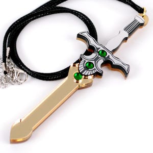 May include: A gold and silver sword pendant necklace with green gems. The sword has a black cord.