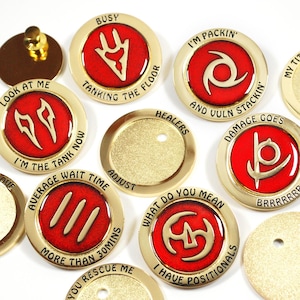 Può includere: Una collezione di spille in metallo color oro con centri in smalto rosso. Ogni spilla presenta un design e un testo unici, tra cui frasi come "Busy", "Tanking the Floor" e "Damage Goes". Le spille sono probabilmente per un gioco o un hobby.