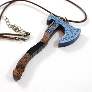 May include: A wooden axe necklace with a blue and silver painted blade and intricate carvings on the handle. The necklace is made of brown cord.