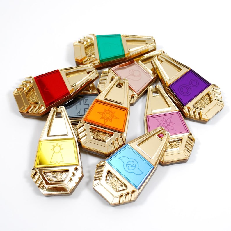 May include: A set of nine gold-colored keychains with different colored translucent inserts. Each keychain features a unique symbol and design.