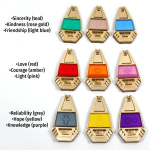 May include: Nine gold-colored charms with different colored glass inserts. Each charm has a different symbol and text describing the meaning of the charm. The text includes: Sincerity (teal), Kindness (rose gold), Friendship (light blue), Love (red), Courage (amber), Light (pink), Reliability (grey), Hope (yellow), and Knowledge (purple).