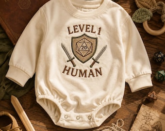Può includere: Un body a maniche lunghe color bianco sporco con un disegno ricamato sul petto. Il ricamo include il testo "LEVEL 1 HUMAN" in marrone, un'icona centrale a forma di scudo con un dado a venti facce e due spade incrociate sotto lo scudo.