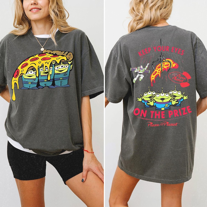 May include: A charcoal gray short-sleeve t-shirt featuring a graphic of three green aliens holding a slice of pizza on the front. The back displays the same aliens, Buzz Lightyear, a claw, and the text KEEP YOUR EYES ON THE PRIZE.