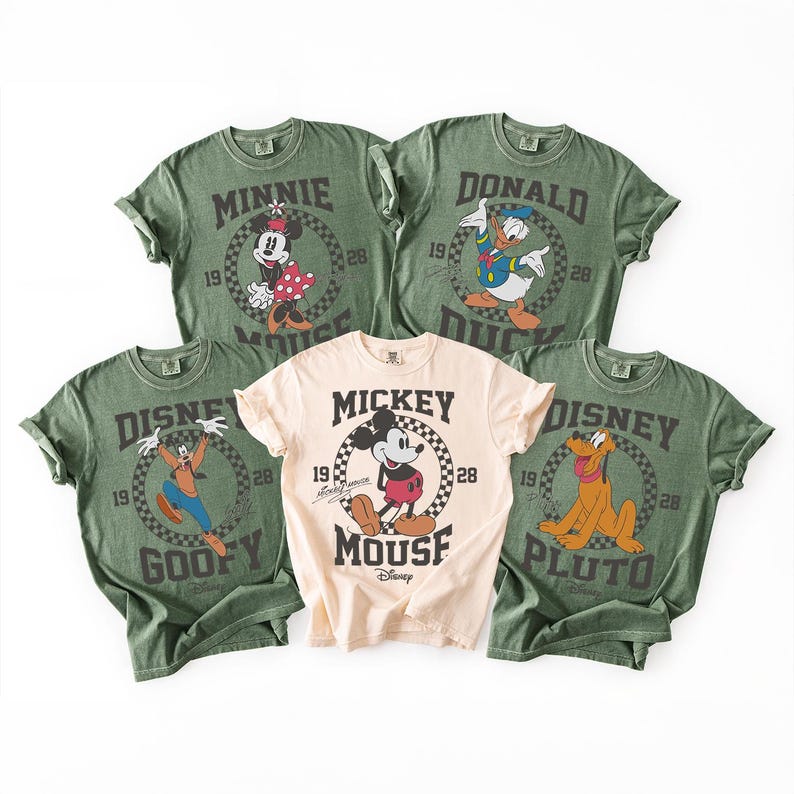 Op de afbeelding: Vijf T-shirts met korte mouwen en ronde hals met Disney-figuren. Vier shirts zijn olijfgroen met afbeeldingen van Minnie Mouse, Donald Duck, Goofy en Pluto. E&eacute;n centraal shirt is cr&egrave;me met een Mickey Mouse-afbeelding en tekst.