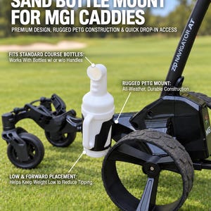 May include: A white PETG sand bottle mount attached to a black MGI Zip Navigator AT golf caddy. The mount features a cylindrical holder for standard course bottles. Text on the image reads: SAND BOTTLE MOUNT FOR MGI CADDIES, PREMIUM DESIGN, RUGGED PETG CONSTRUCTION & QUICK DROP-IN ACCESS, FITS STANDARD COURSE BOTTLES, RUGGED PETG MOUNT, LOW & FORWARD PLACEMENT, BOTTLE OPTIONAL.