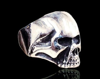 Può includere: Un anello a forma di teschio in argento con un design dettagliato. L'anello è su uno sfondo nero con il testo "Ezi Zino Handmade Jewelry".