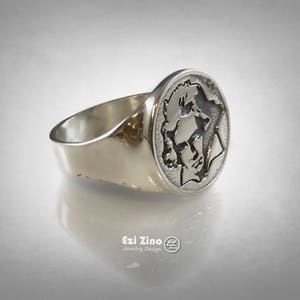 Op de afbeelding: Een zilveren ring met een rond, gegraveerd ontwerp met een profiel van een gezicht. De ring is gemaakt van gepolijst zilver en heeft een gladde, afgeronde band.