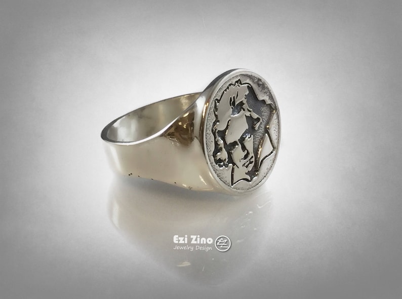 Op de afbeelding: Een zilveren ring met een rond, gegraveerd ontwerp met een profiel van een gezicht. De ring is gemaakt van gepolijst zilver en heeft een gladde, afgeronde band.