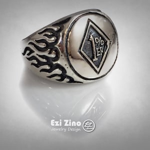 May include: A silver ring with a black and white diamond-shaped design featuring the text "1%ER" inside. The ring has a silver band with a flame design.