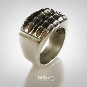 May include: A silver ring with a textured, geometric design on the top. The ring is marked with the number "25".