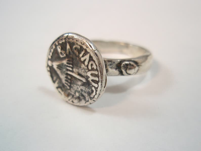 May include: A silver ring with a coin-shaped design featuring a bird and the inscription "& CIVIS".