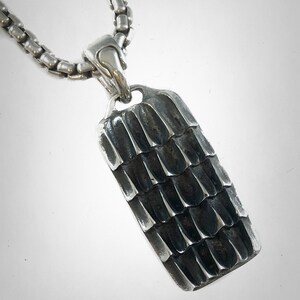 May include: A silver chain necklace with a silver pendant. The pendant is rectangular and has a textured surface. The pendant is about 2 inches long and 1 inch wide.