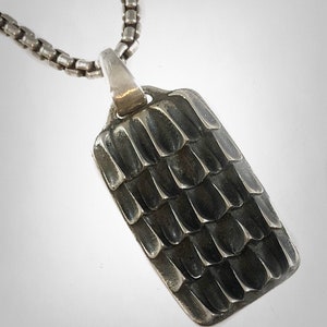 May include: A silver pendant necklace with a textured rectangular pendant. The pendant has a pattern of small, raised squares.