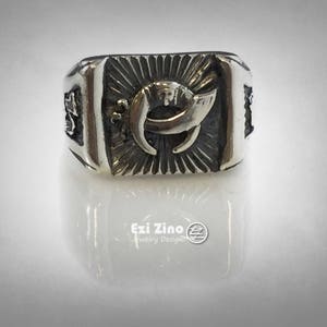 Puede incluir: Un anillo de plata con un dise&ntilde;o detallado que presenta una luna creciente y rayos de sol. El anillo est&aacute; grabado con las palabras "Ezi Zino Jewelry Designs".
